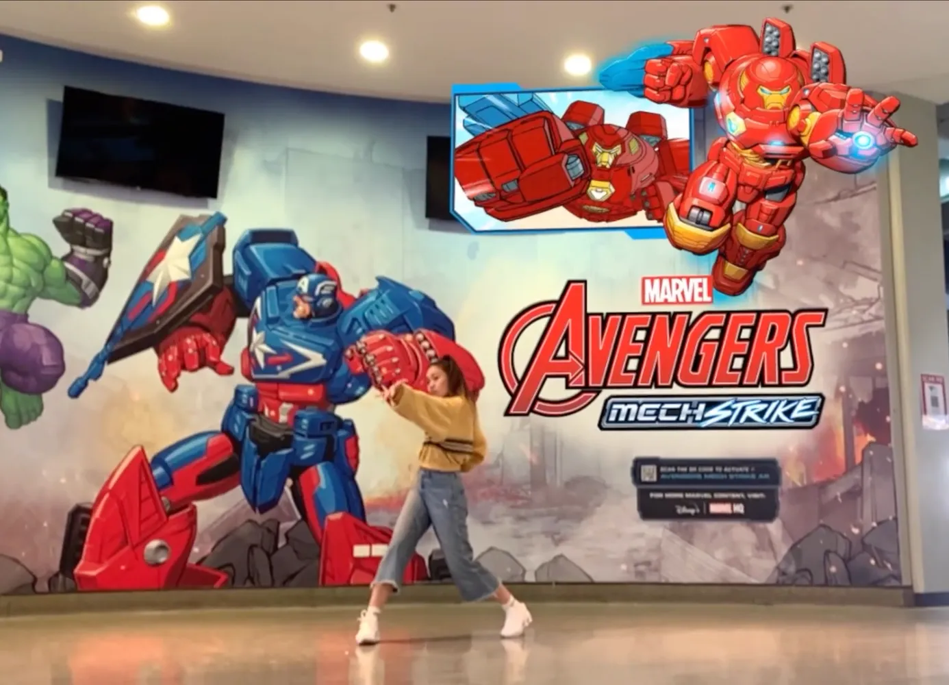 Woman standing infront of Disney Mech Strike promotional poster with AR Iron Man in background.